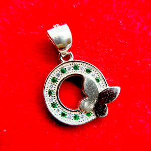 A silver pendant with a circular design featuring green gemstones and a white butterfly motif