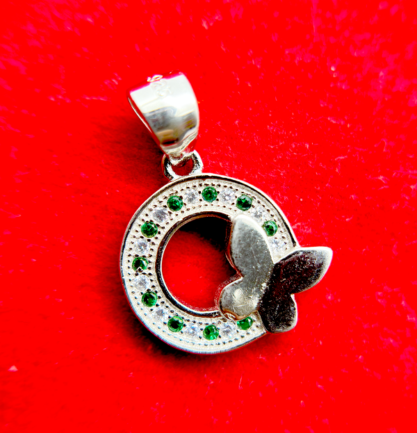 A silver pendant with a circular design featuring green gemstones and a white butterfly motif