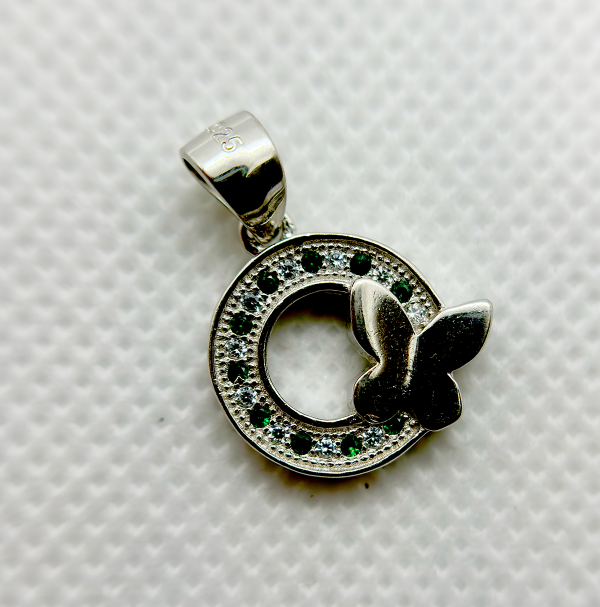 A silver pendant with a circular design featuring green gemstones and a white butterfly motif