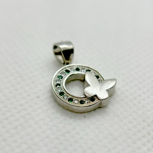 A silver pendant with a circular design featuring green gemstones and a white butterfly motif