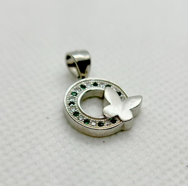 A silver pendant with a circular design featuring green gemstones and a white butterfly motif