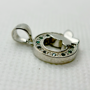 A silver pendant with a circular design featuring green gemstones and a white butterfly motif