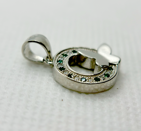 A silver pendant with a circular design featuring green gemstones and a white butterfly motif