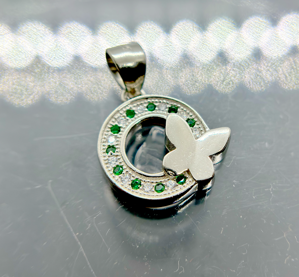 A silver pendant with a circular design featuring green gemstones and a white butterfly motif