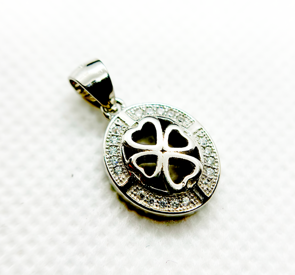 Close-up of a silver pendant with a heart-shaped cutout and a clover design, encrusted with small diamonds