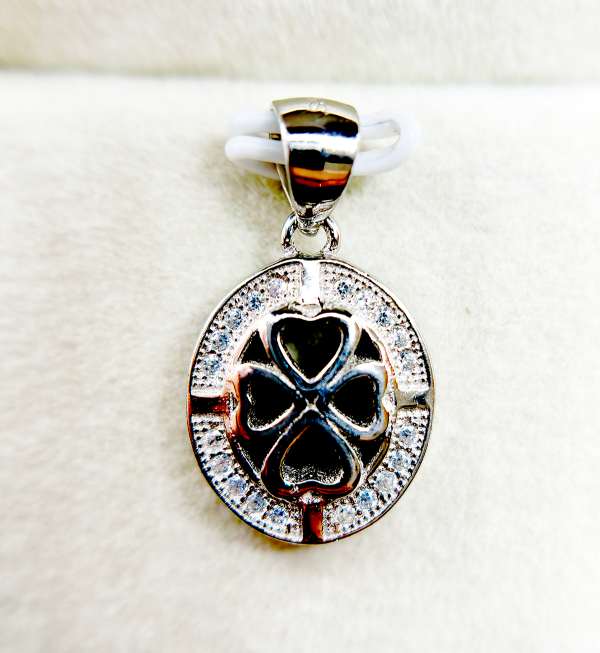 Close-up of a silver pendant with a heart-shaped cutout and a clover design, encrusted with small diamonds