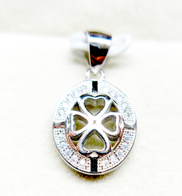 Close-up of a silver pendant with a heart-shaped cutout and a clover design, encrusted with small diamonds