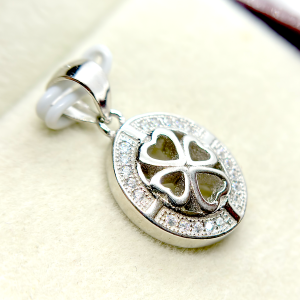 Close-up of a silver pendant with a heart-shaped cutout and a clover design, encrusted with small diamonds