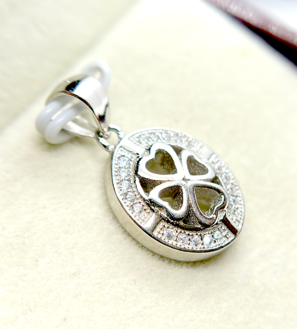 Close-up of a silver pendant with a heart-shaped cutout and a clover design, encrusted with small diamonds