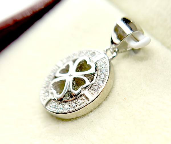 Close-up of a silver pendant with a heart-shaped cutout and a clover design, encrusted with small diamonds