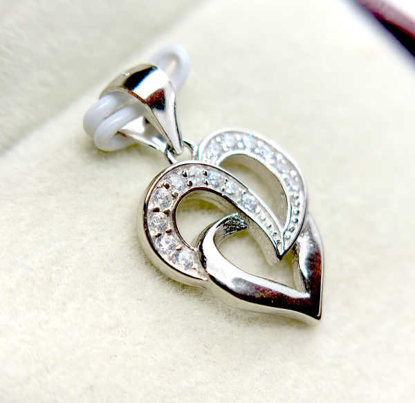 A silver heart-shaped pendant with an intertwined design and small diamond