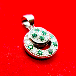 A circular pendant with green and clear gemstones set in a silver