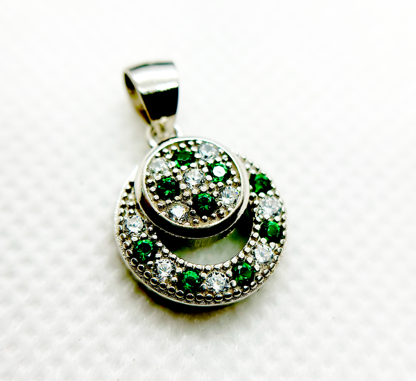 A circular pendant with green and clear gemstones set in a silver