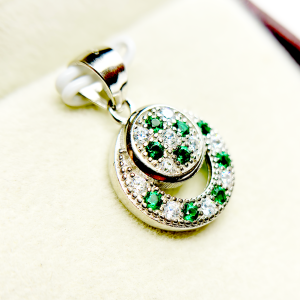 A circular pendant with green and clear gemstones set in a silver