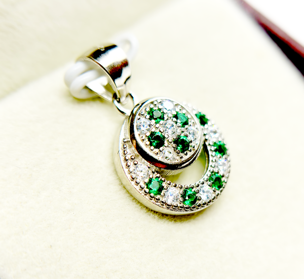 A circular pendant with green and clear gemstones set in a silver