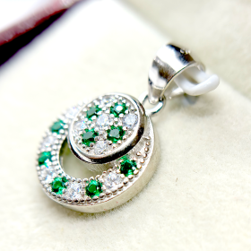 A circular pendant with green and clear gemstones set in a silver